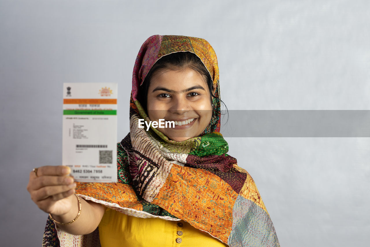 one person, smiling, portrait, adult, happiness, women, looking at camera, clothing, young adult, holding, yellow, studio shot, emotion, indoors, cheerful, traditional clothing, smile, teeth, front view, gray background, copy space, lifestyles, gray, waist up, female, standing, person, headshot, scarf