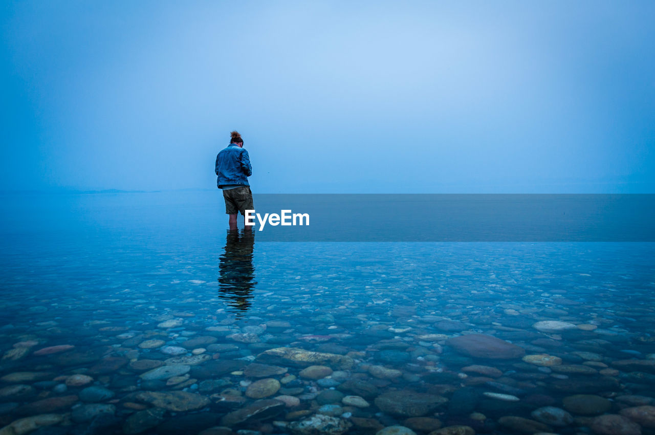 Rear view of man standing in sea against blue sky