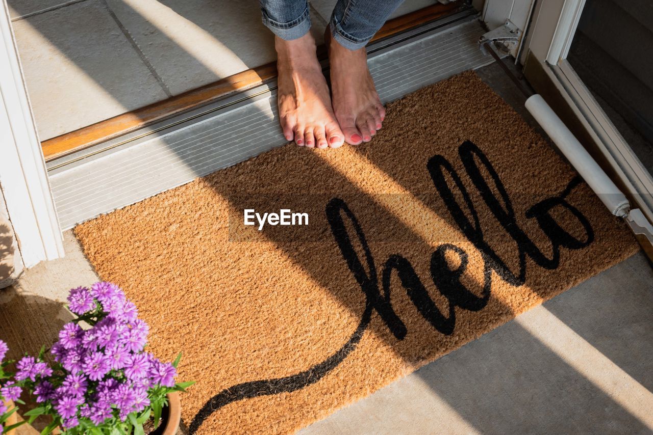 Low section of woman standing by doormat with hello text