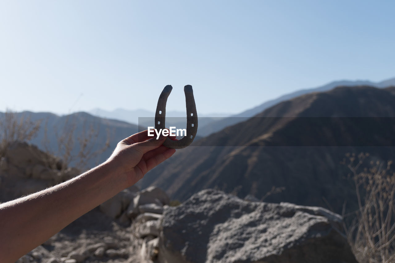 Cropped hand holding horseshoe against mountains