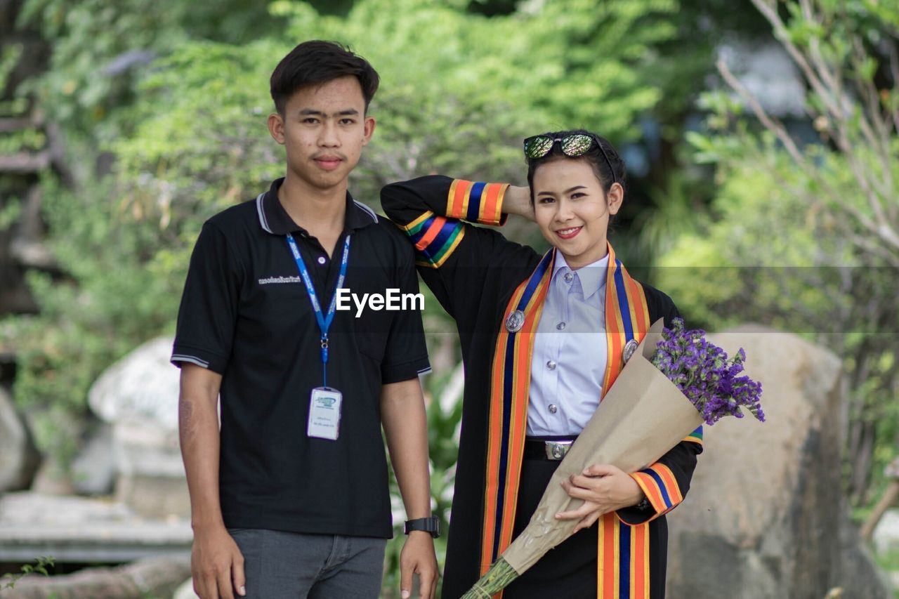 PORTRAIT OF SMILING YOUNG COUPLE STANDING OUTDOORS