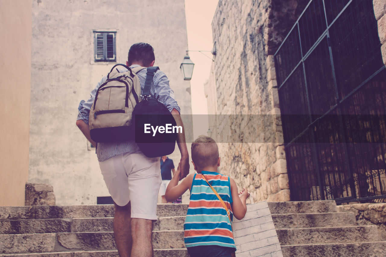 Rear view of father and son holding hands while climbing on steps in city