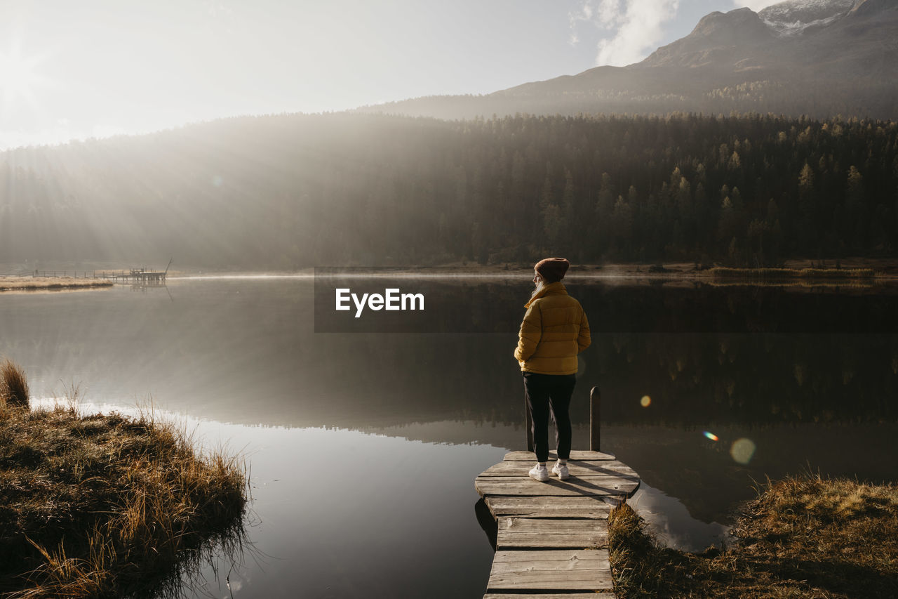 Switzerland, engadine, lake staz, woman standing on a jetty at lakeside in morning sun