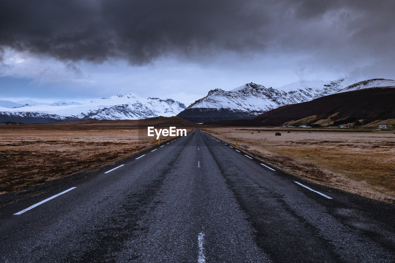 Empty road leading towards snowcapped mountains against sky