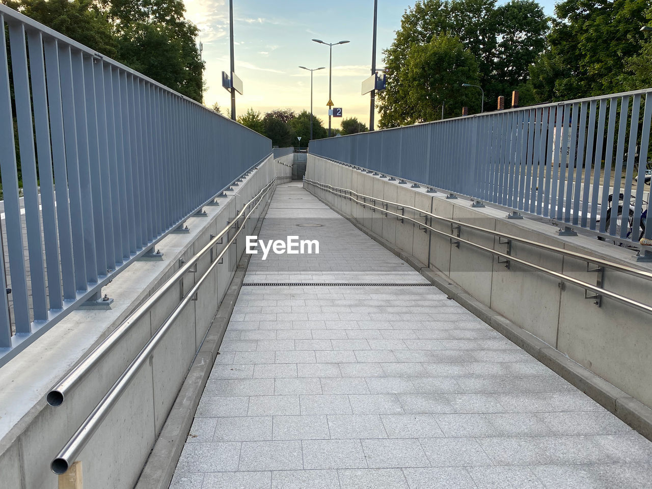 architecture, walkway, built structure, railing, footpath, tree, plant, city, the way forward, nature, sky, diminishing perspective, bridge, day, transportation, handrail, no people, outdoors, street, building exterior, footbridge, outdoor structure, sidewalk, pedestrian walkway, road