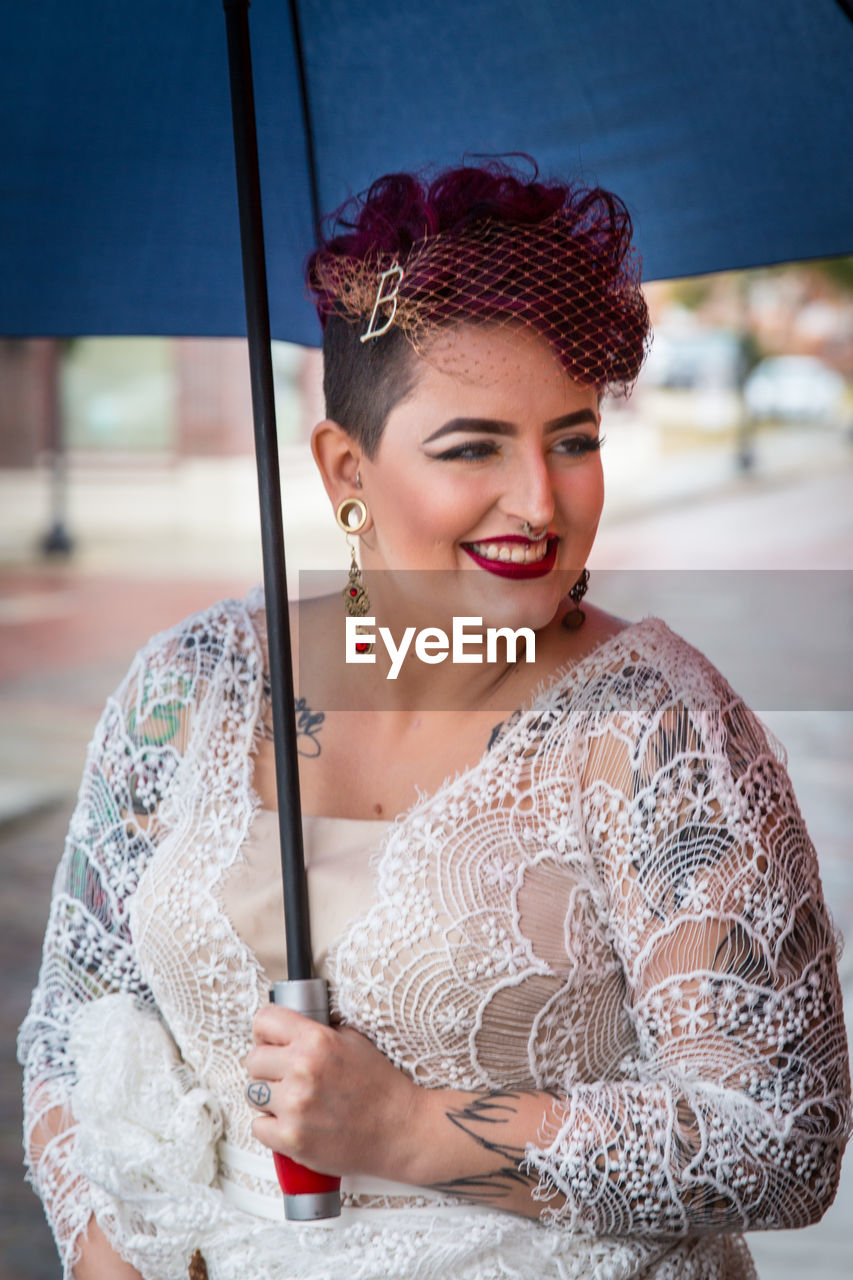 Smiling woman in costume holding blue umbrella at event