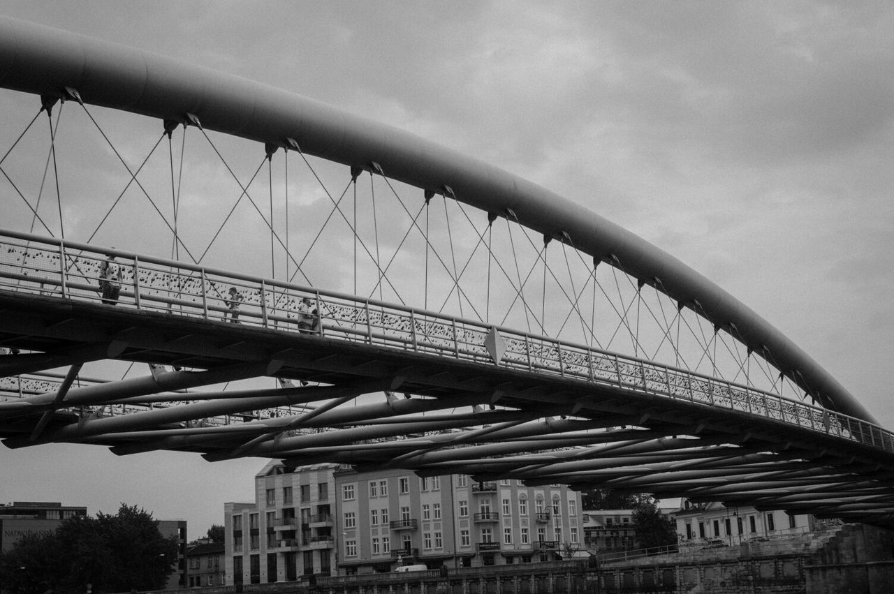 Low angle view of pedestrian walkway bridge against cloudy sky