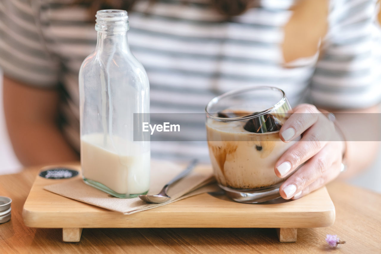 MIDSECTION OF WOMAN HOLDING GLASS OF TABLE