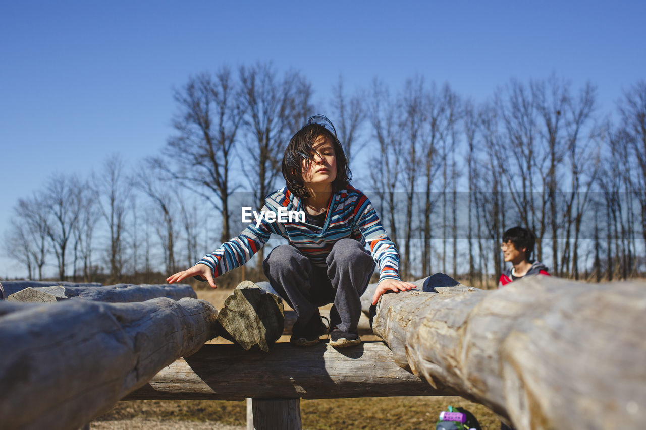 A child perches on wooden structure in park with father in background
