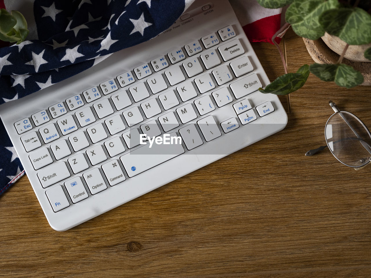Flat lay photo of computer keyboard, us flag, eyeglasses and greenery on wooden table