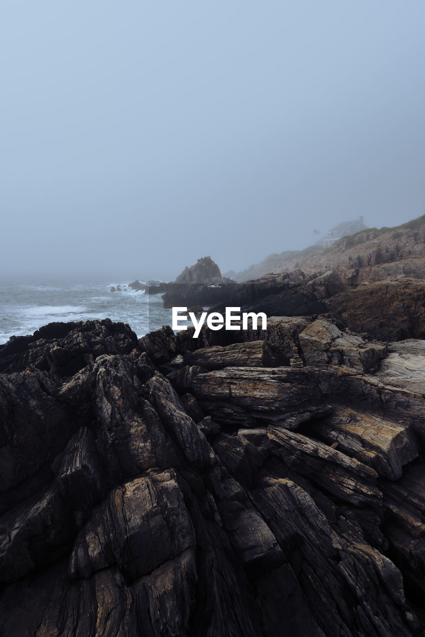 Scenic view of rocks at beach against sky during foggy weather