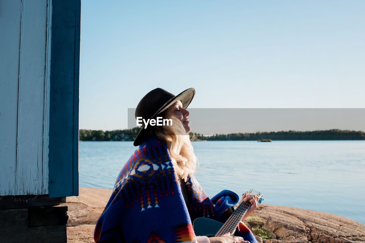 Woman sat taking in vitamin d whilst playing the guitar at the beach