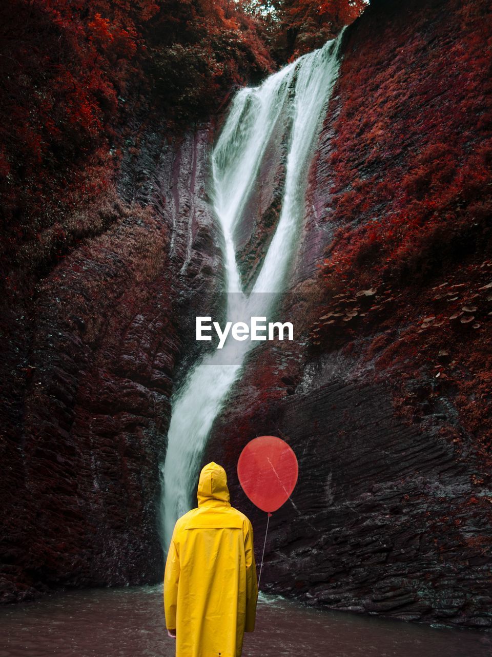 Rear view of person holding balloon against waterfall