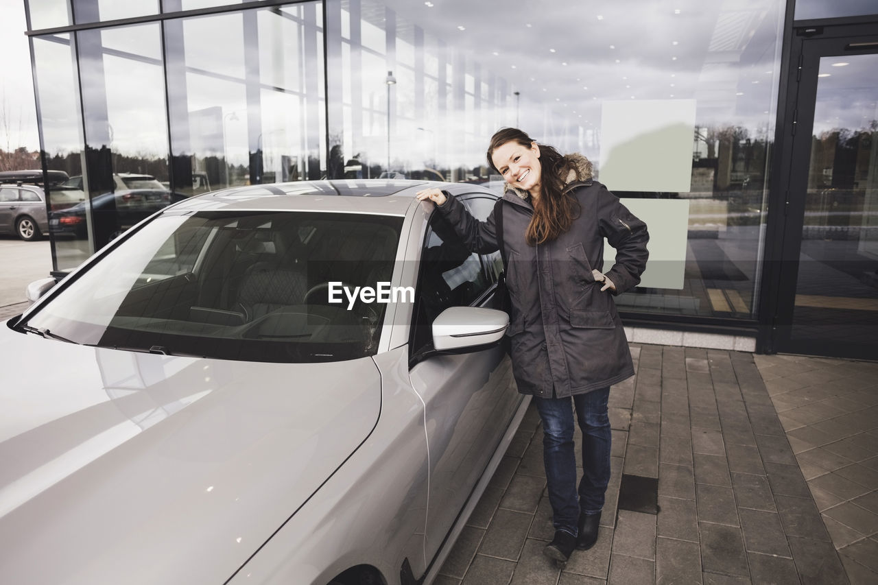 Portrait of smiling woman standing by car against showroom