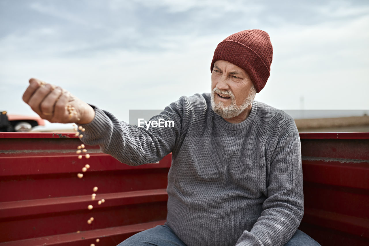 Farmer wearing knit hat examining cultivated soybean against clear sky