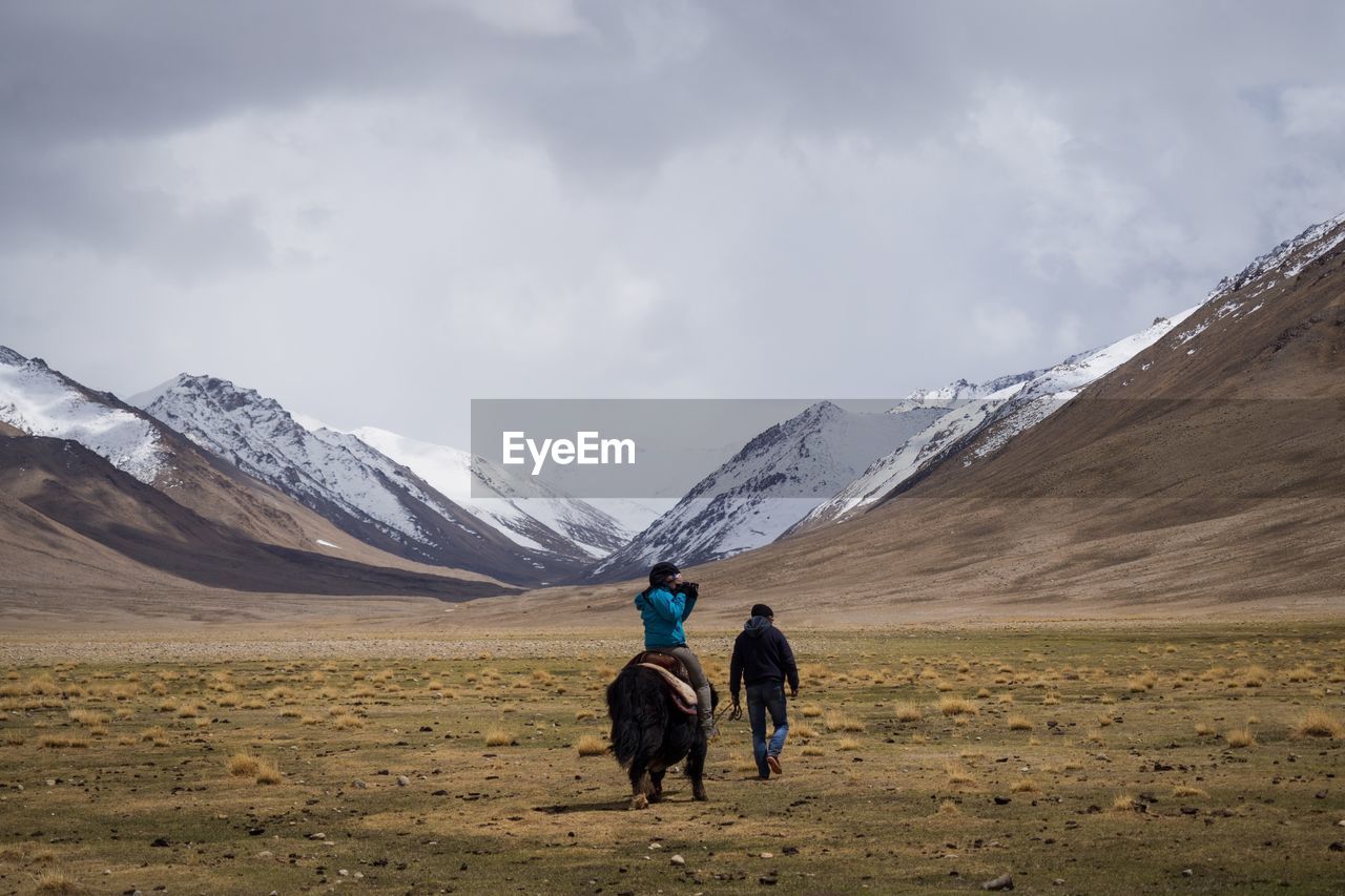 REAR VIEW OF MEN WITH SNOWCAPPED MOUNTAIN AGAINST SKY