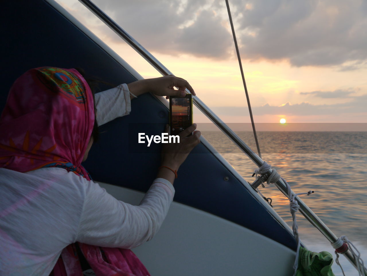 Woman photographing sunset over sea through smart phone while travelling in boat