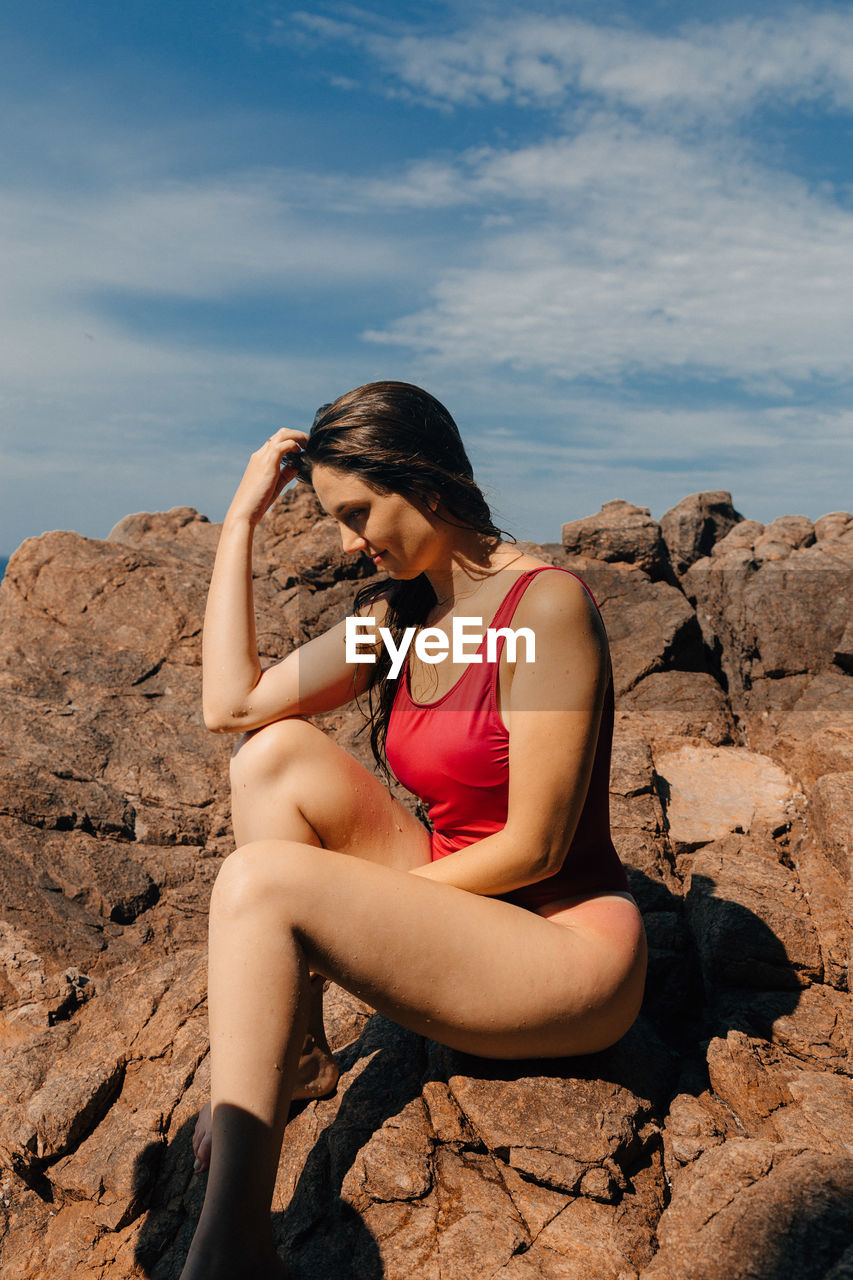 Sensuous woman sitting on rock against sky