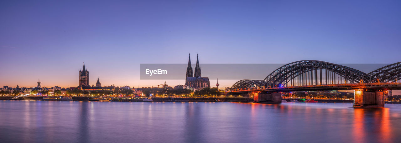 Illuminated bridge over river against sky in city at dusk