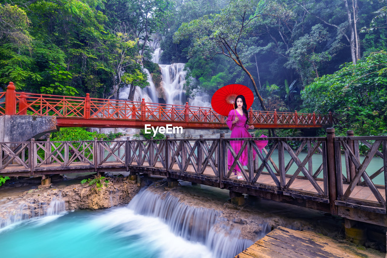 Young asian woman in pink dress walking on wooden path in kuang si waterfall 