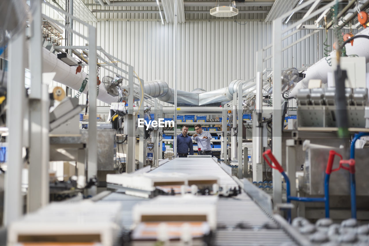 Two men talking at conveyor belt in factory shop floor