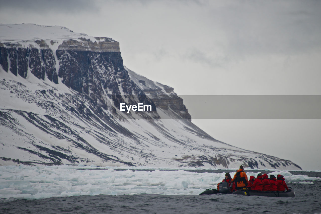 People rafting in river by snowcapped mountain against sky