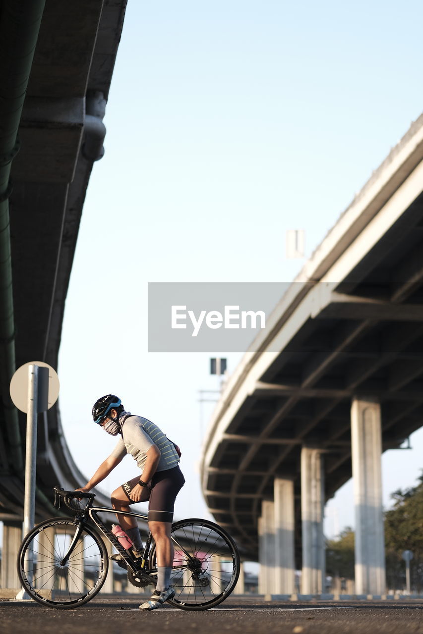 Man riding bicycle under bridge against clear sky