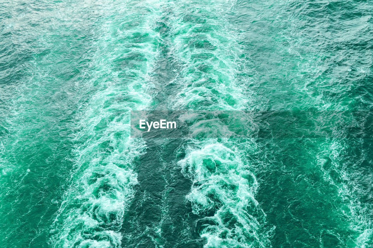 Stormy foam and a ship's track on the turquoise sea water.