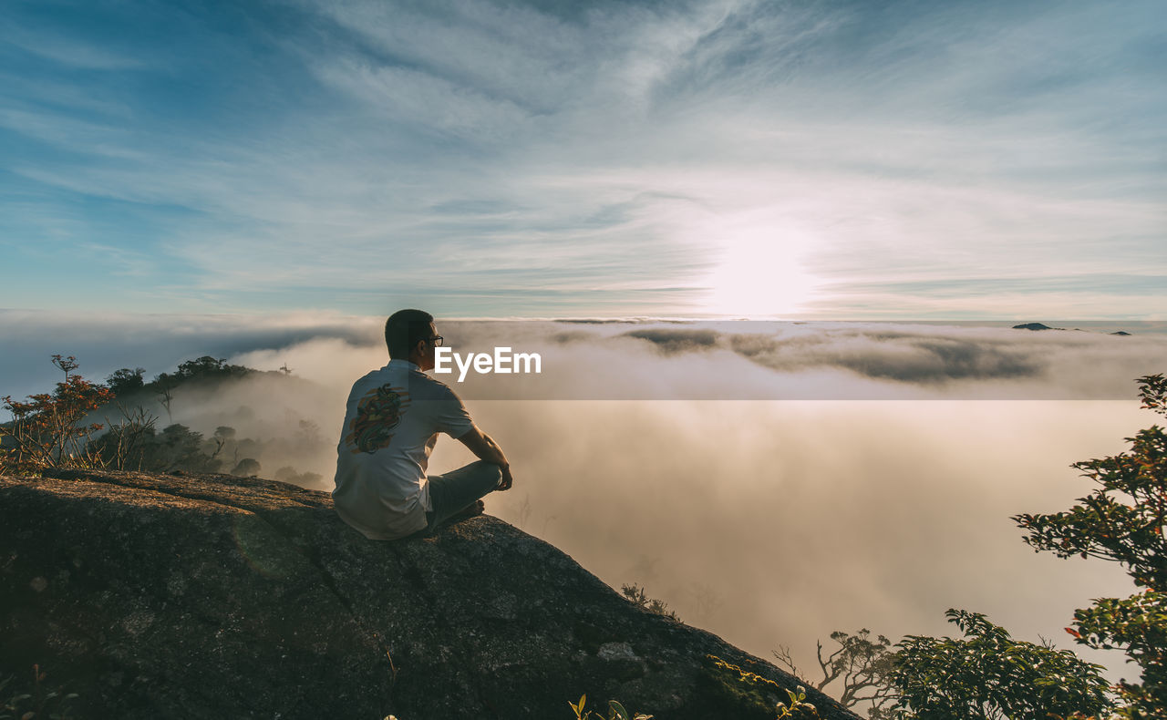 Side view of man standing on rock against sky