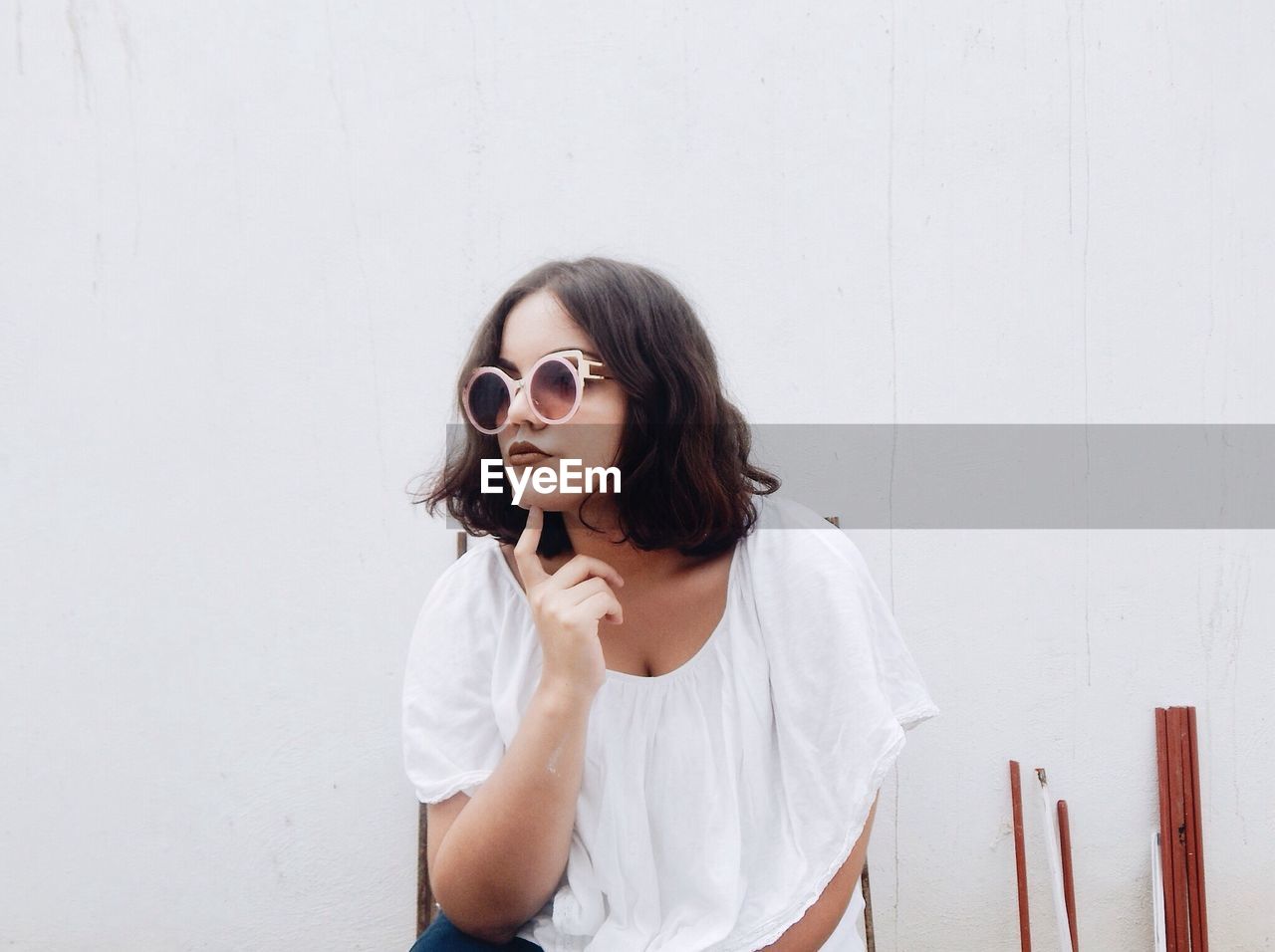 Woman wearing sunglasses posing against white wall