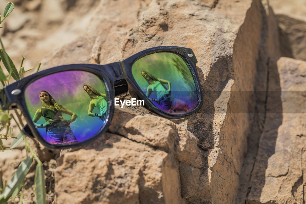 High angle view of sunglasses on rock with reflection of beautiful young women. 