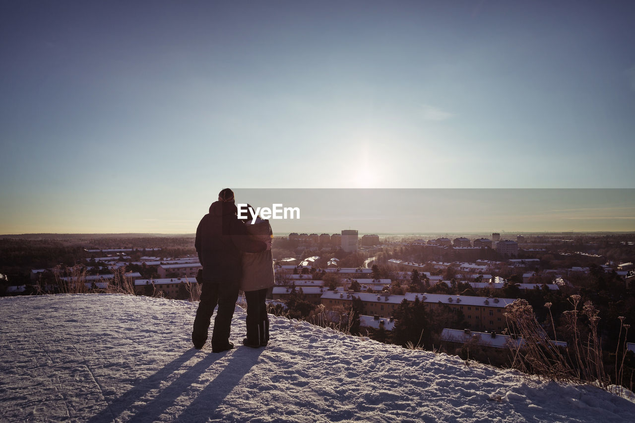 Full length rear view of couple embracing while standing on mountain during winter