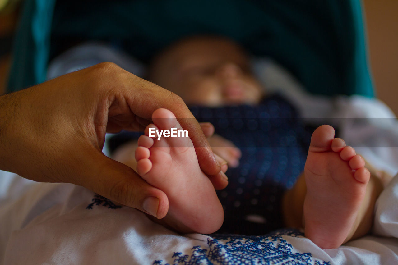 Cropped mother hand holding baby leg on bed at home