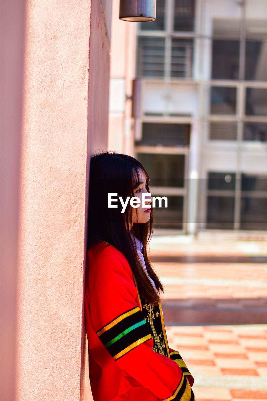 Side view of young woman standing against wall against building