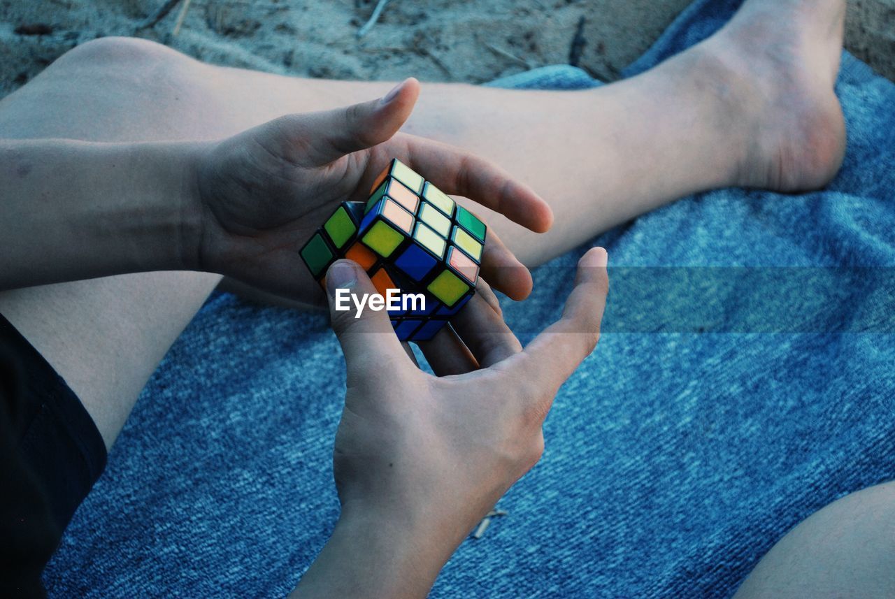 Low section of man holding puzzle cube while sitting at beach