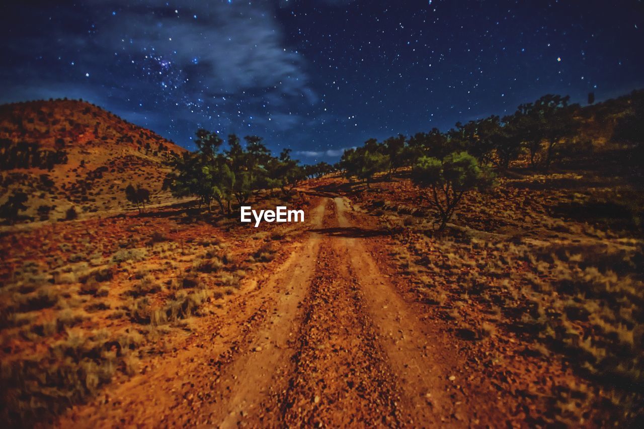 ROAD AMIDST LANDSCAPE AGAINST STAR FIELD AT NIGHT