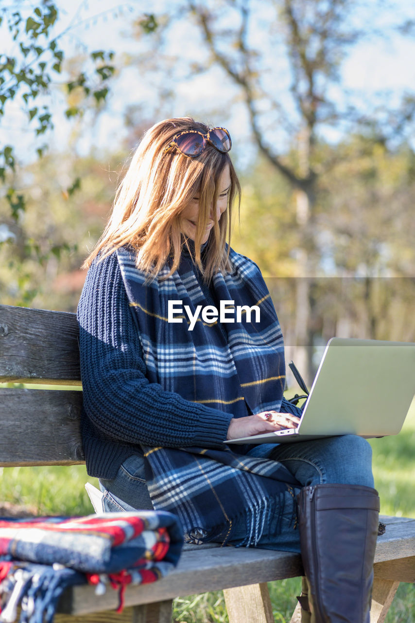 Mature woman using laptop while sitting on bench in park