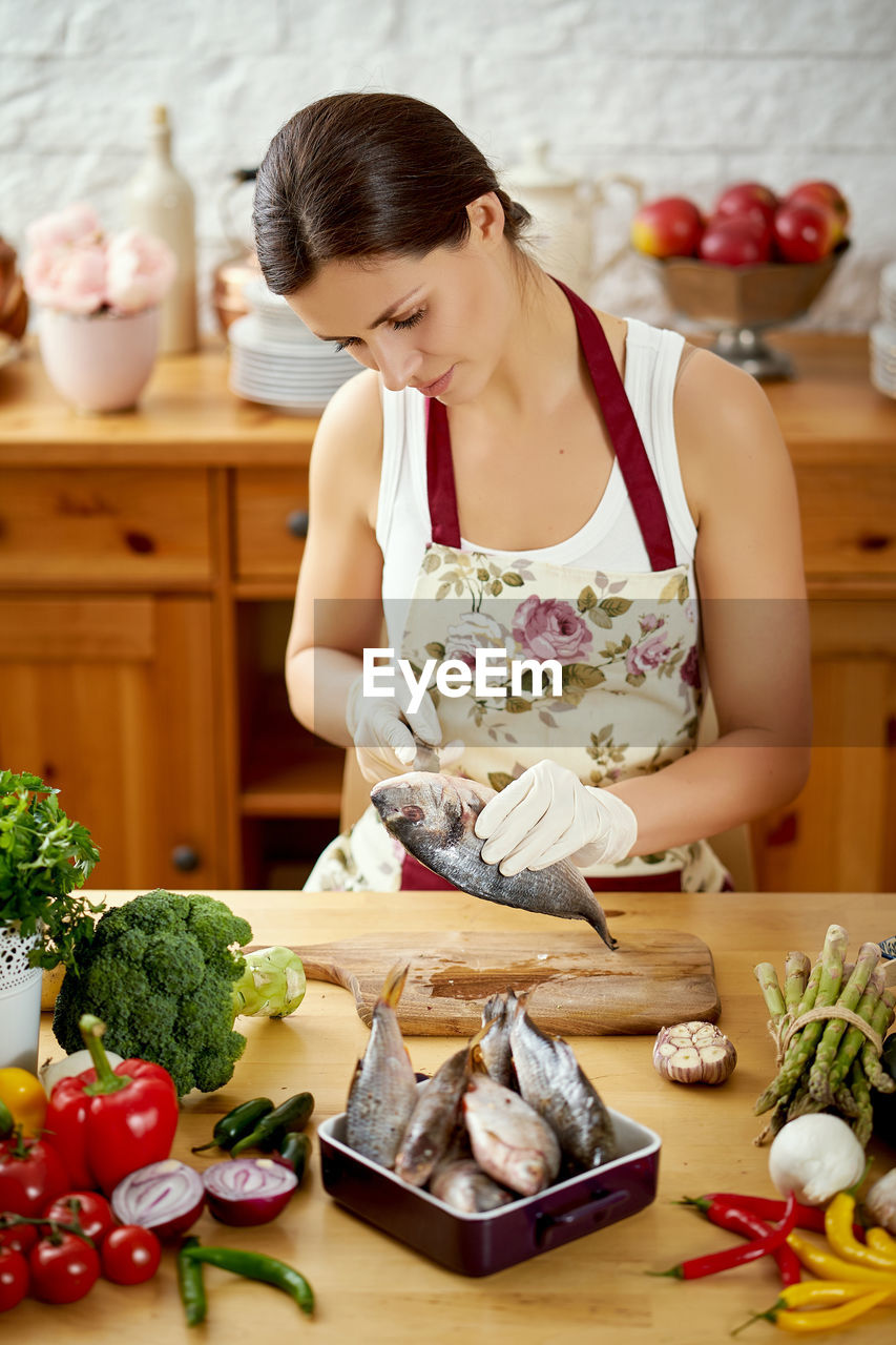 Beautiful woman cleaning fish in kitchen