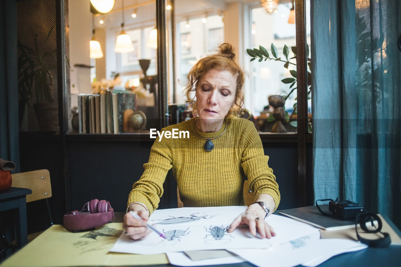 Confident mature female illustrator drawing on paper at desk in creative office