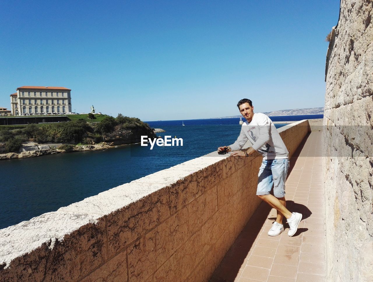 Full length portrait of young man standing by sea against clear blue sky