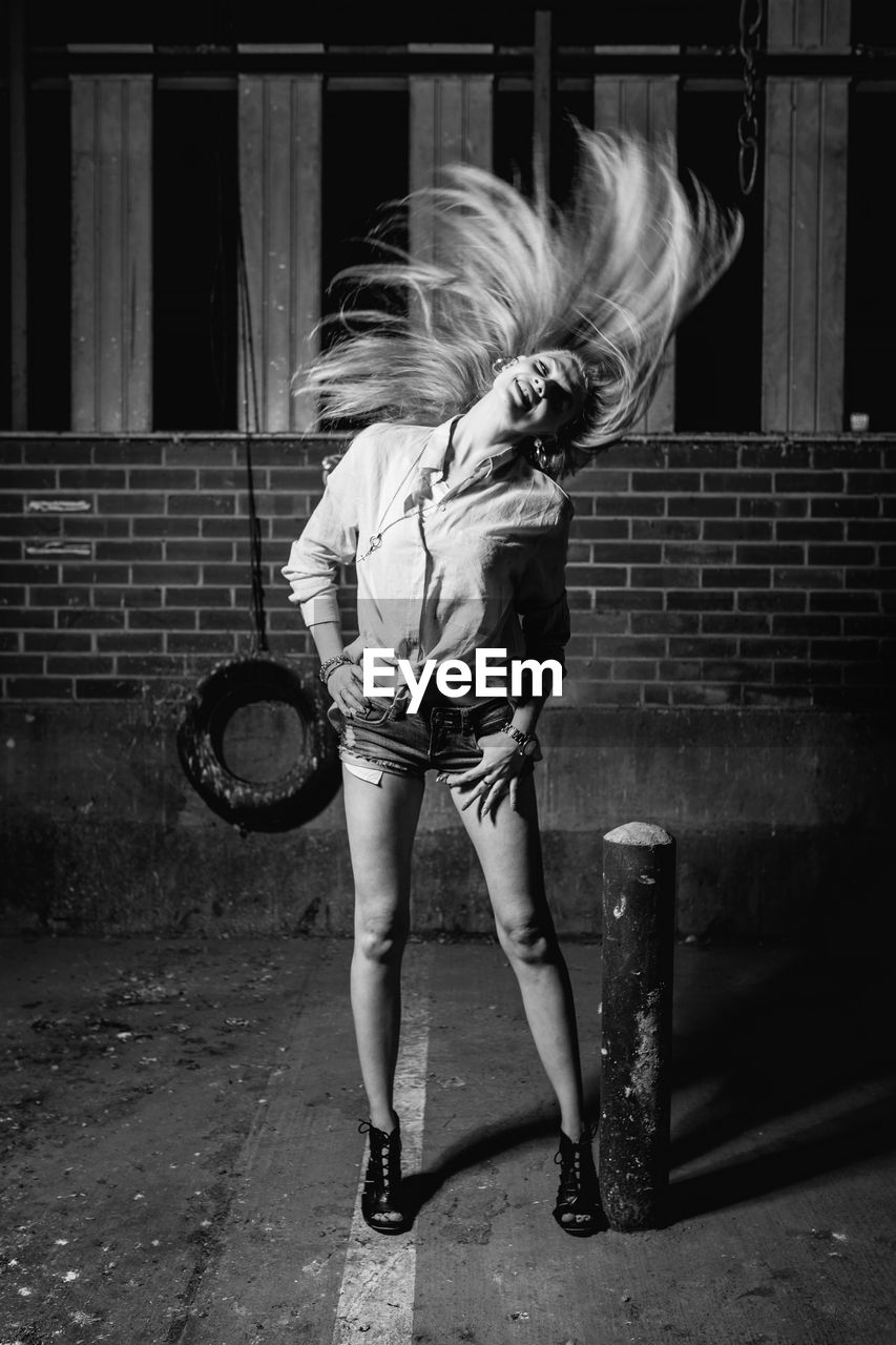 Smiling young woman tossing hair on footpath at night