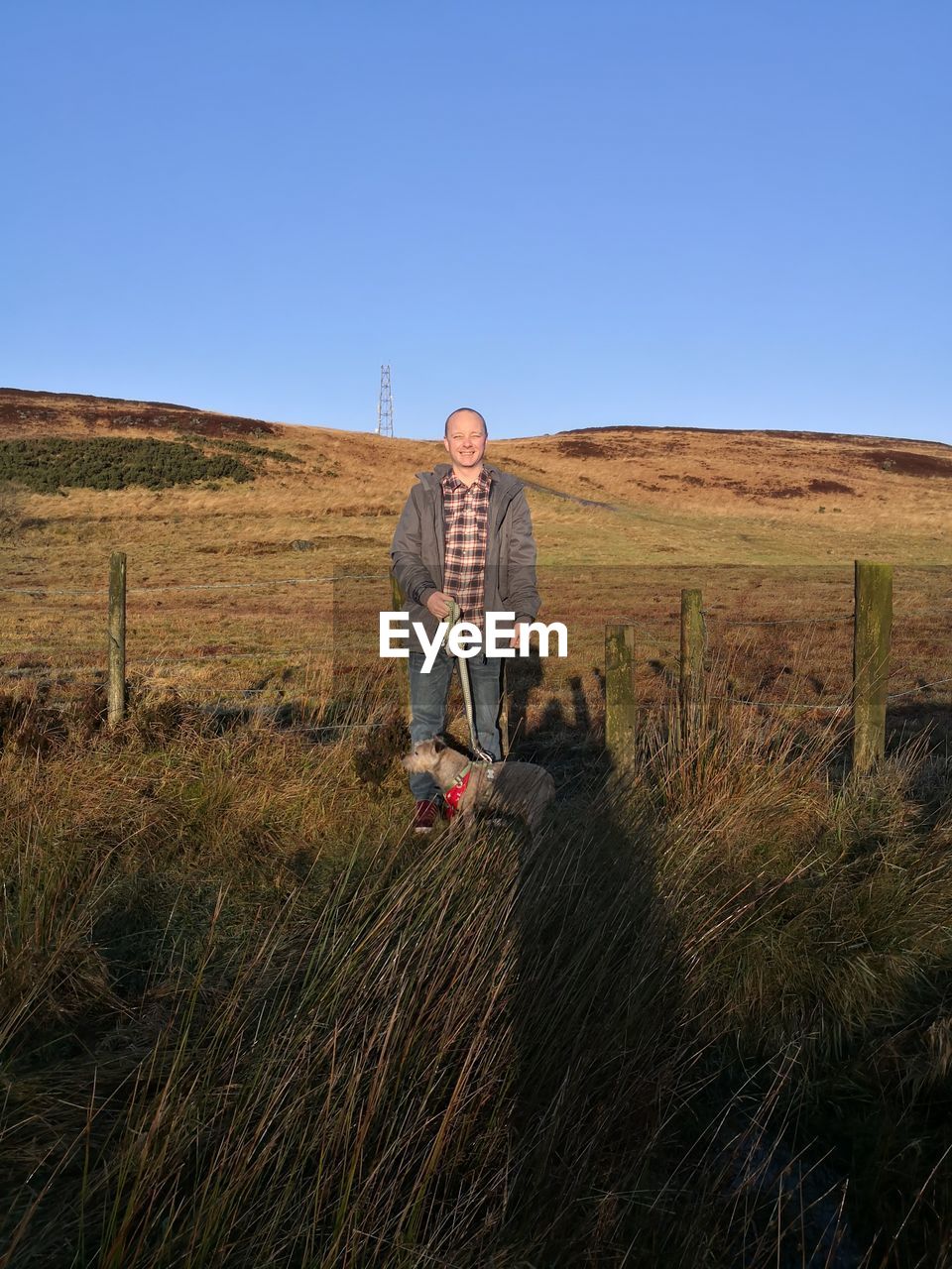 Man with dog by grass against clear sky