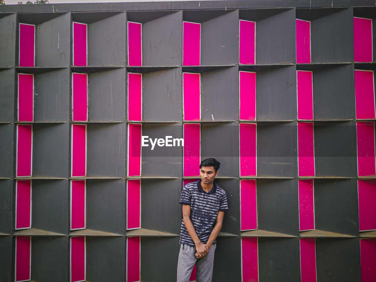 Full length of young man standing against pink wall