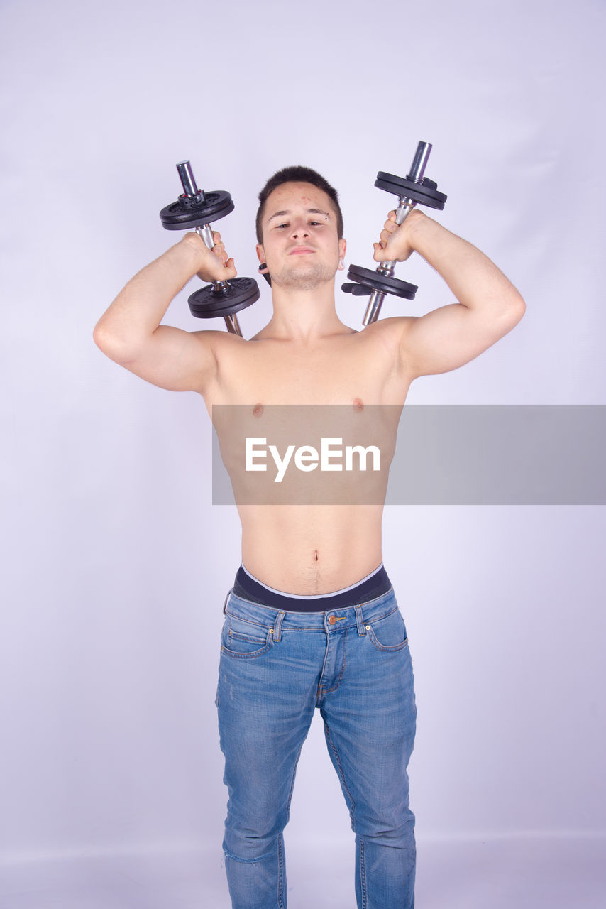 Shirtless man lifting dumbbells against purple background