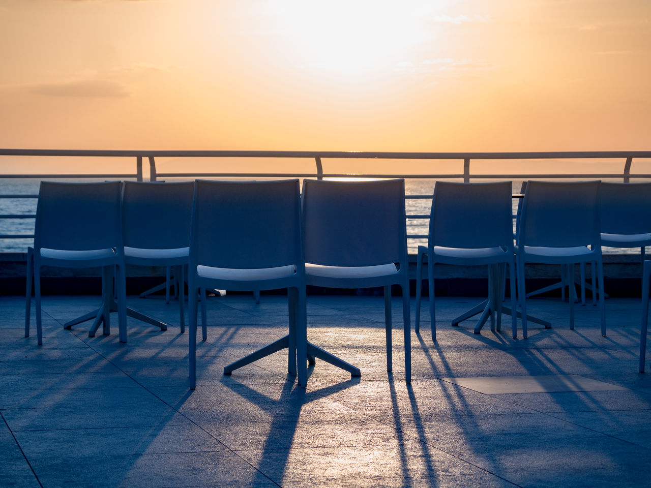 Empty chairs and tables against sky during sunset