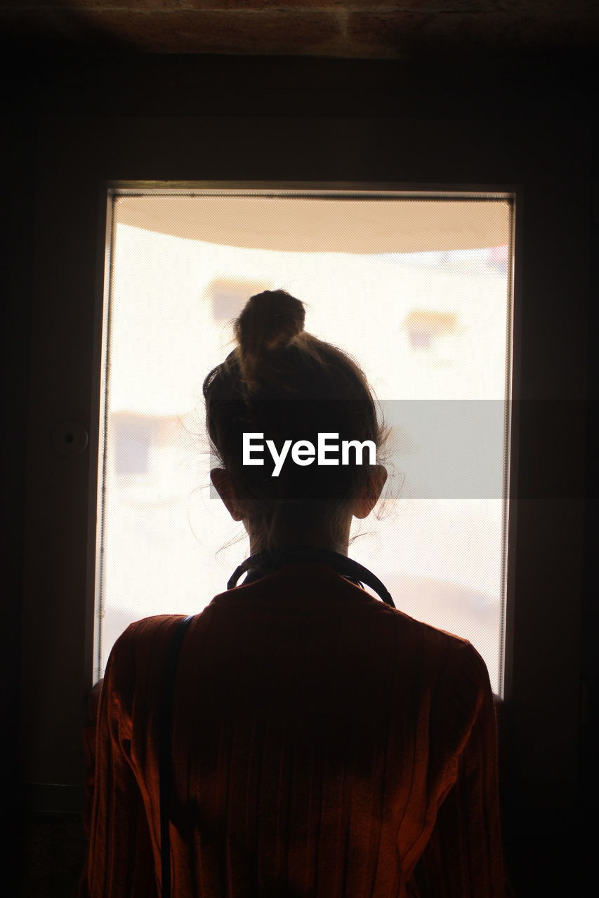 Rear view of woman looking through window at home