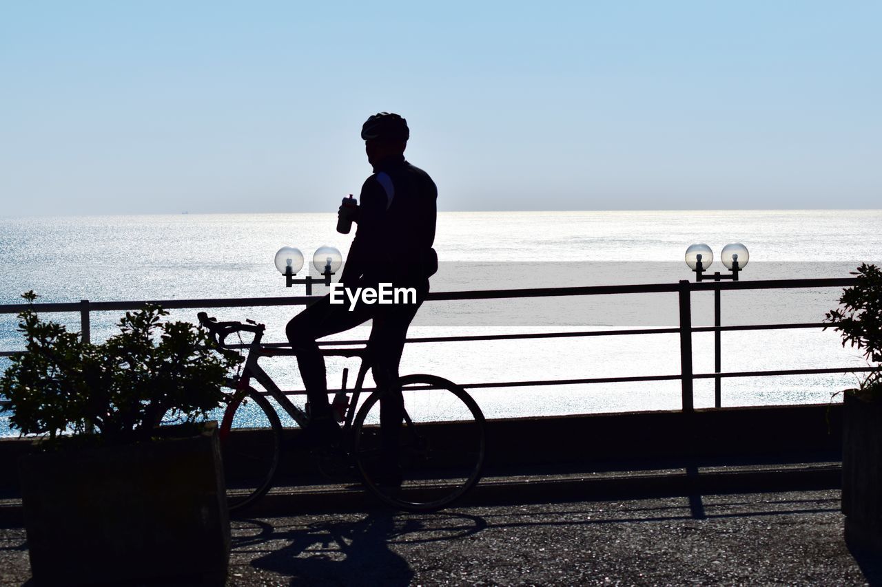 Silhouette man riding bicycle against sea