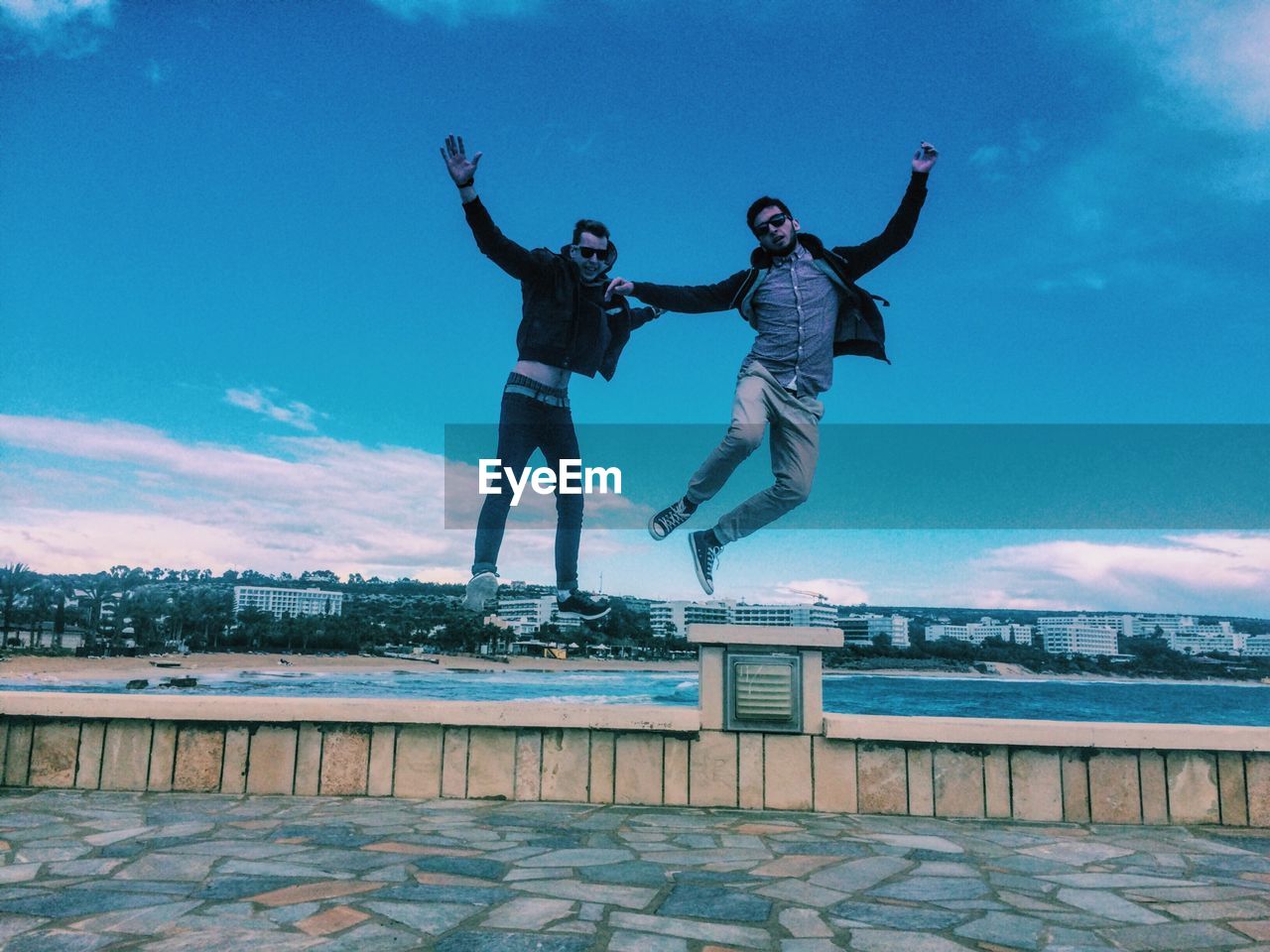 Friends levitating over pavement by beach against sky