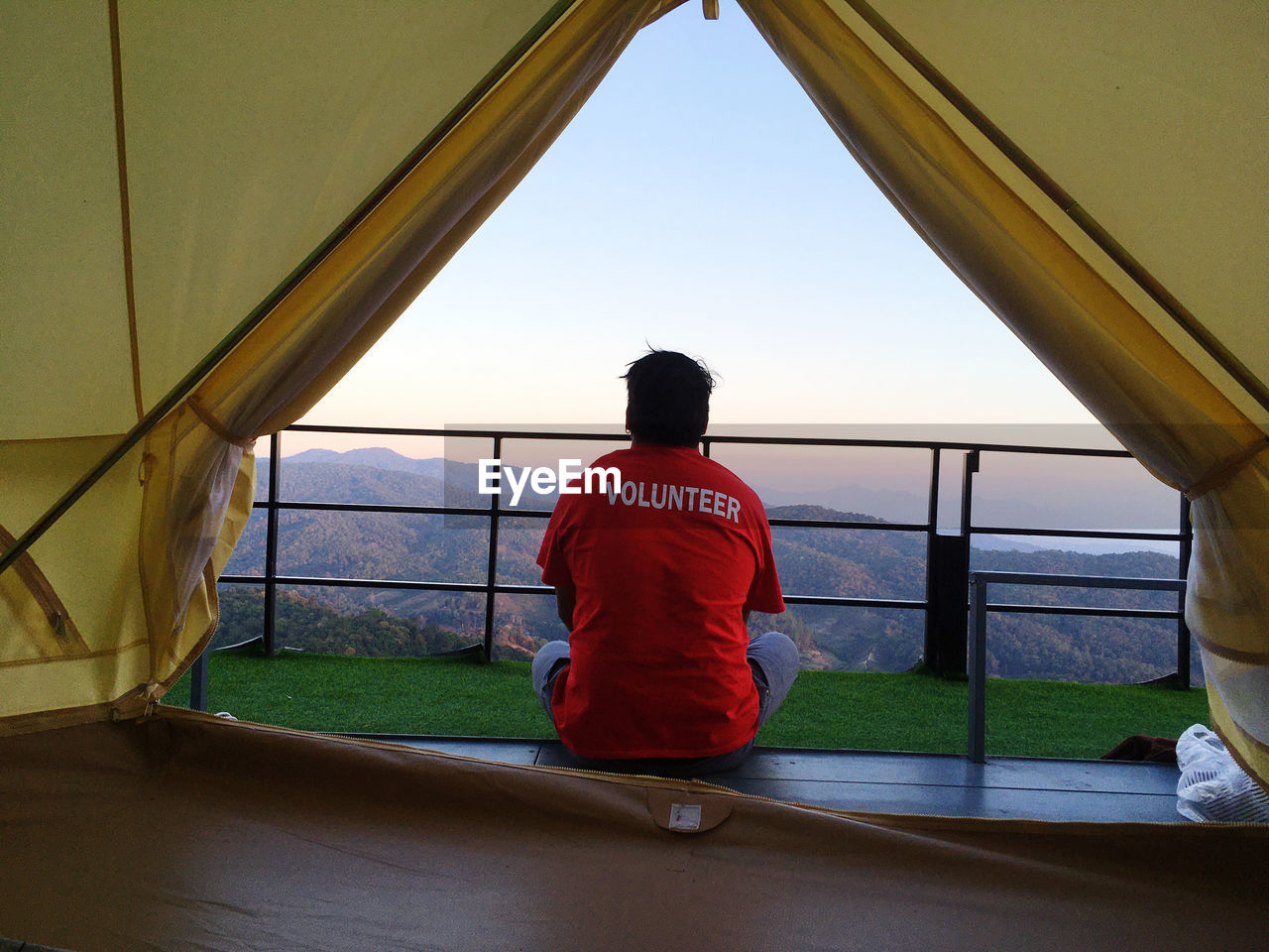 Rear view of man sitting on land seen through tent during sunset