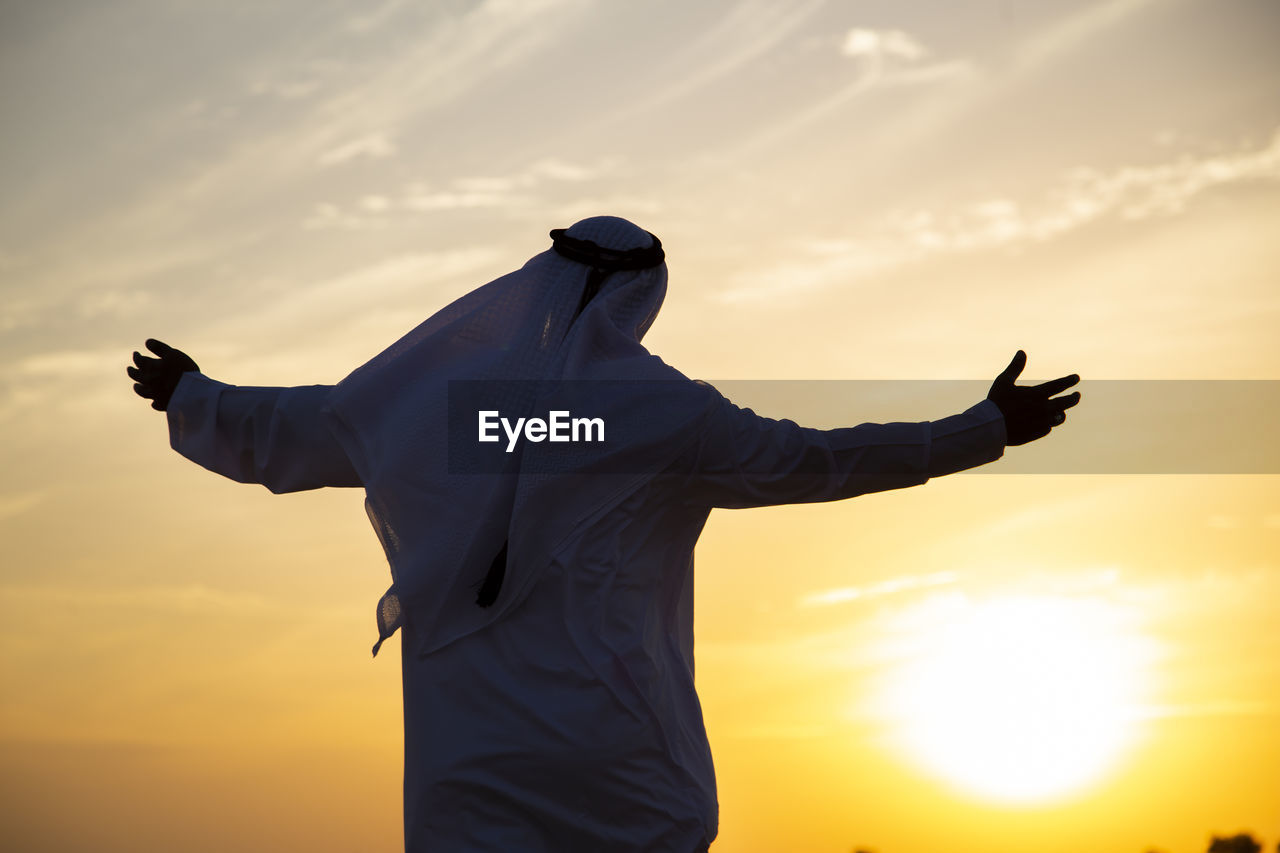 Rear view of man in traditional clothing standing against sky during sunset